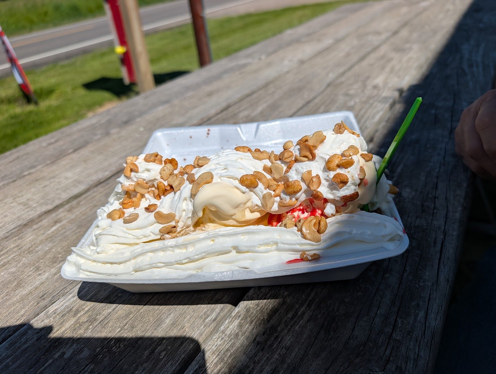 Soft serve sundae piled with whipped cream and peanuts on a picnic table